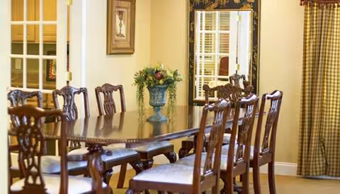 A formal dining room with a long wooden table, ornate chairs, and centerpiece.