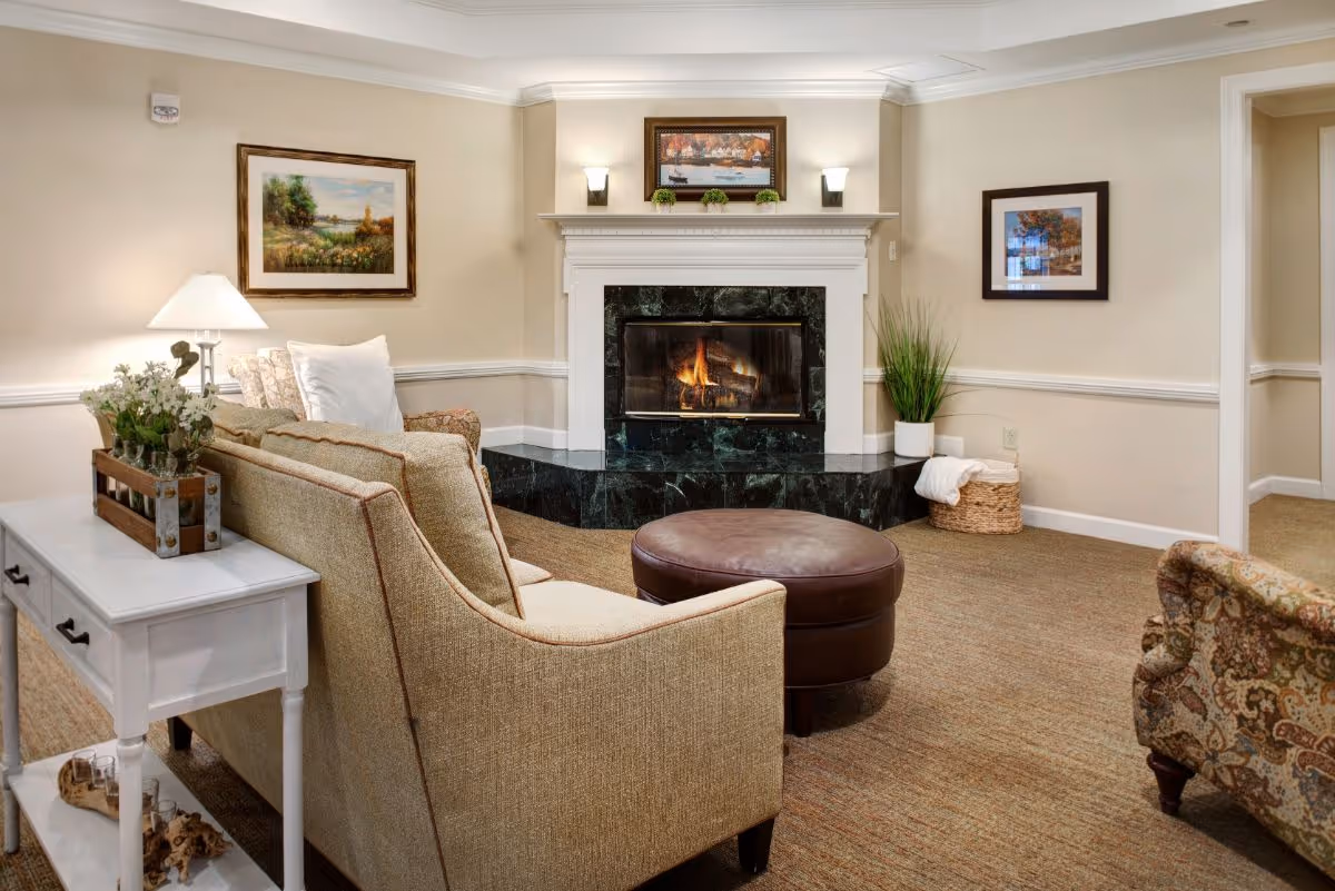 Cozy living room with a lit fireplace, sofa, ottoman, armchairs, and framed artwork.