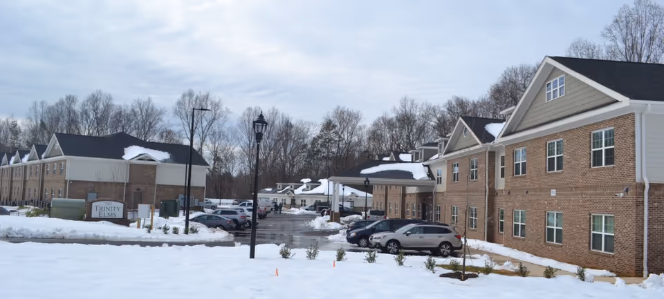 Exterior front view of the Trinity Elms assisted living buildings and parking lot with snow on the ground.