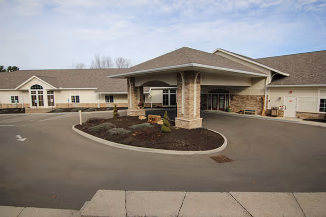 Covered entrance and circular drive of a single-story senior living building with stone pillars and a landscaped island.