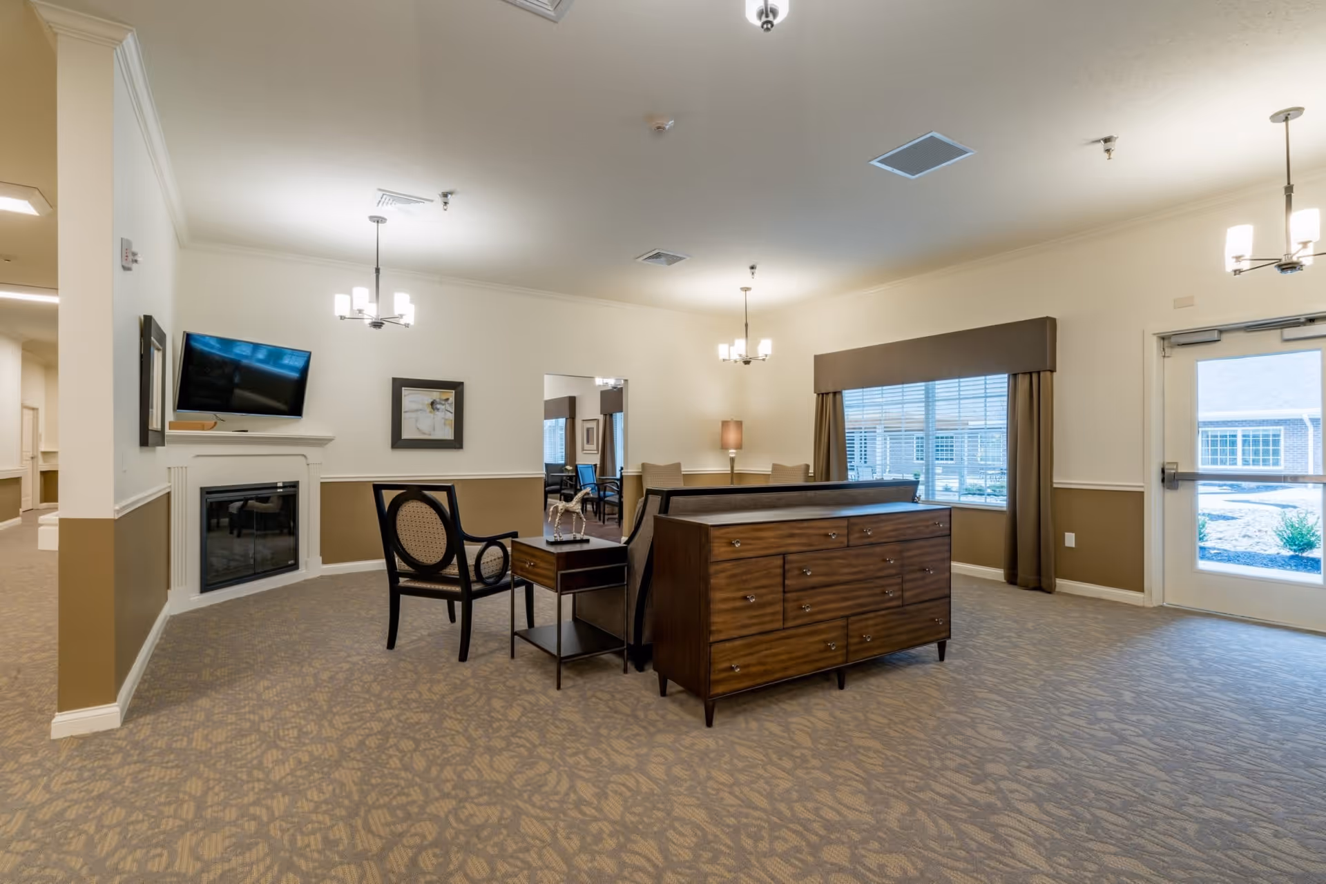 Spacious common lounge with seating, a fireplace, a wall-mounted TV, and a large window by the entrance.