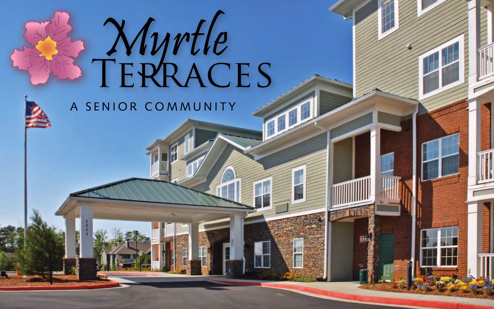 Exterior view of Myrtle Terraces, a senior community building with a covered entrance, multiple windows, and a mix of brick and siding on the facade. An American flag is visible on a flagpole to the left, and there are landscaped areas with flowers and trees.