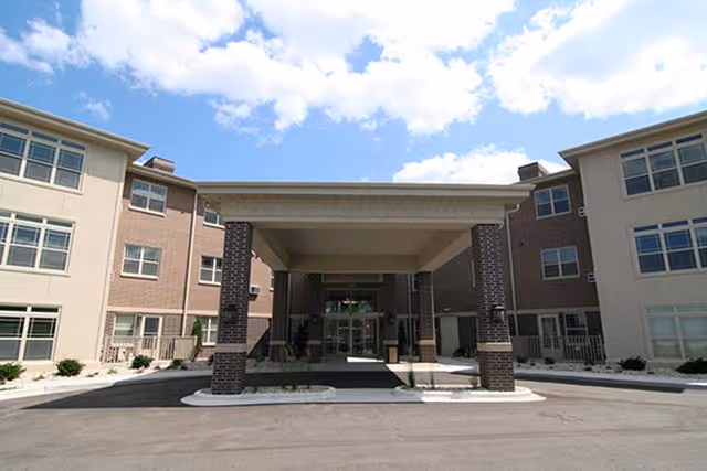Exterior view of Garden Place Apartments entrance with a covered drop-off, brick columns, and clear sky.