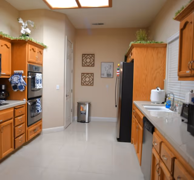 A bright galley kitchen with oak cabinets, double ovens, a stainless refrigerator, and a sink area.