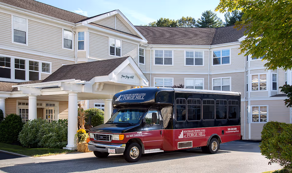 A Forge Hill senior living shuttle bus parked in front of the beige multi-story facility entrance.