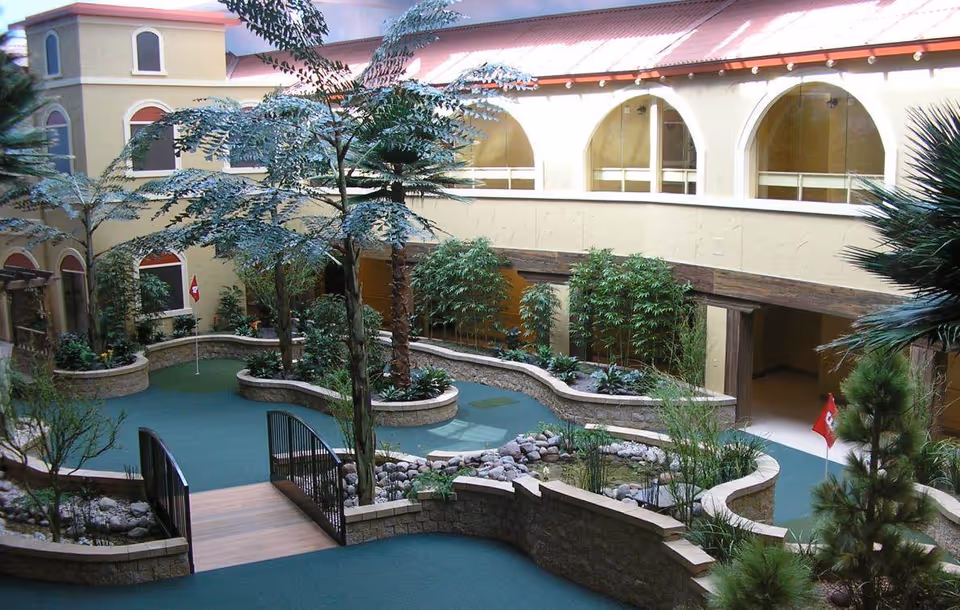 Indoor atrium courtyard with winding planted islands, a small wooden bridge over a water feature, and arched second-floor windows.