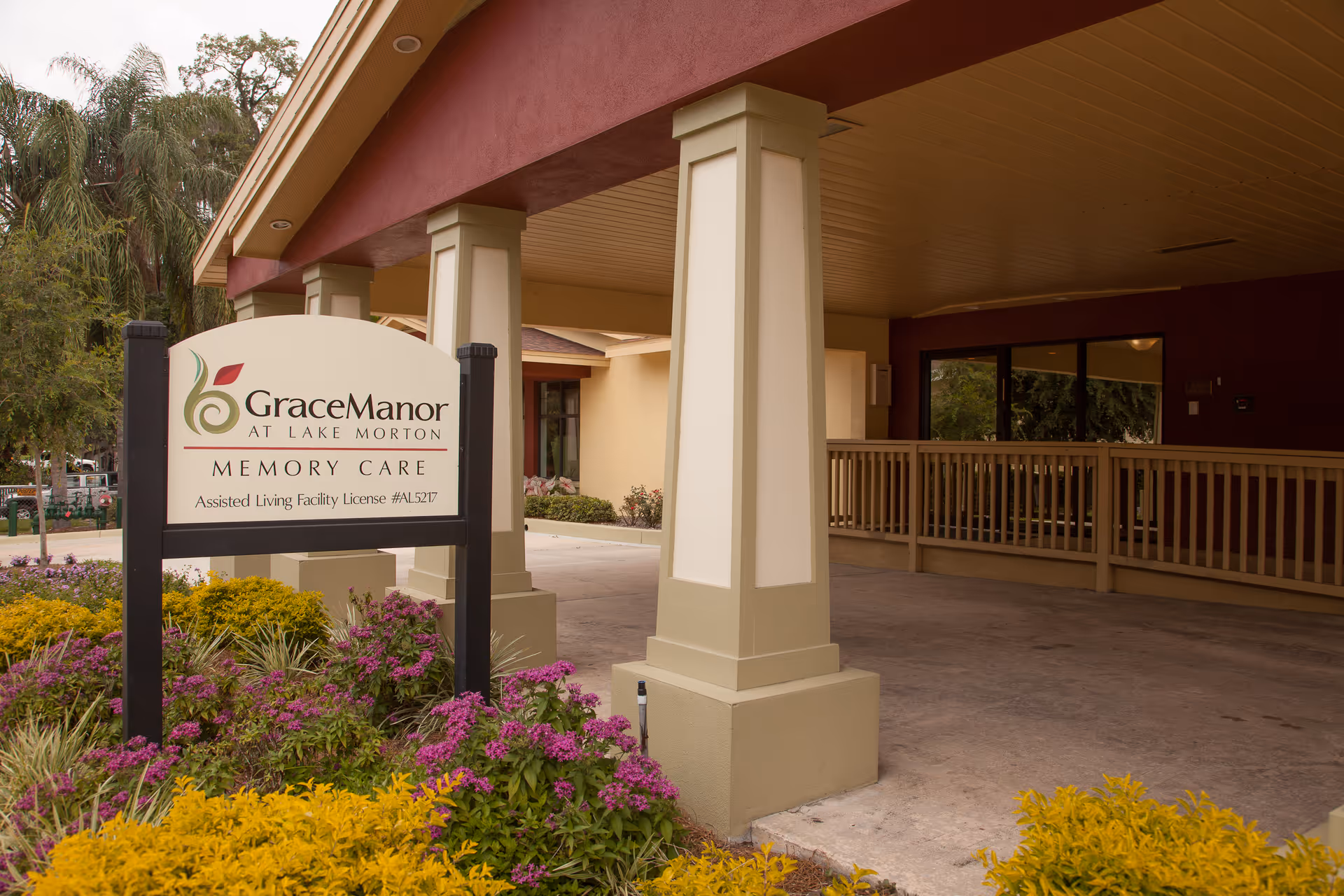 Covered entrance and sign for Grace Manor at Lake Morton Memory Care with pillars and landscaped flowers.
