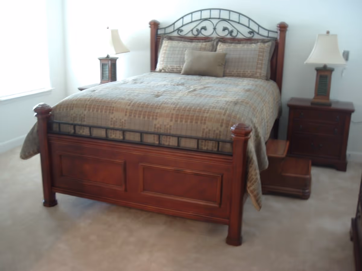 Wooden bed with patterned bedding flanked by two nightstands and lamps in a carpeted bedroom.