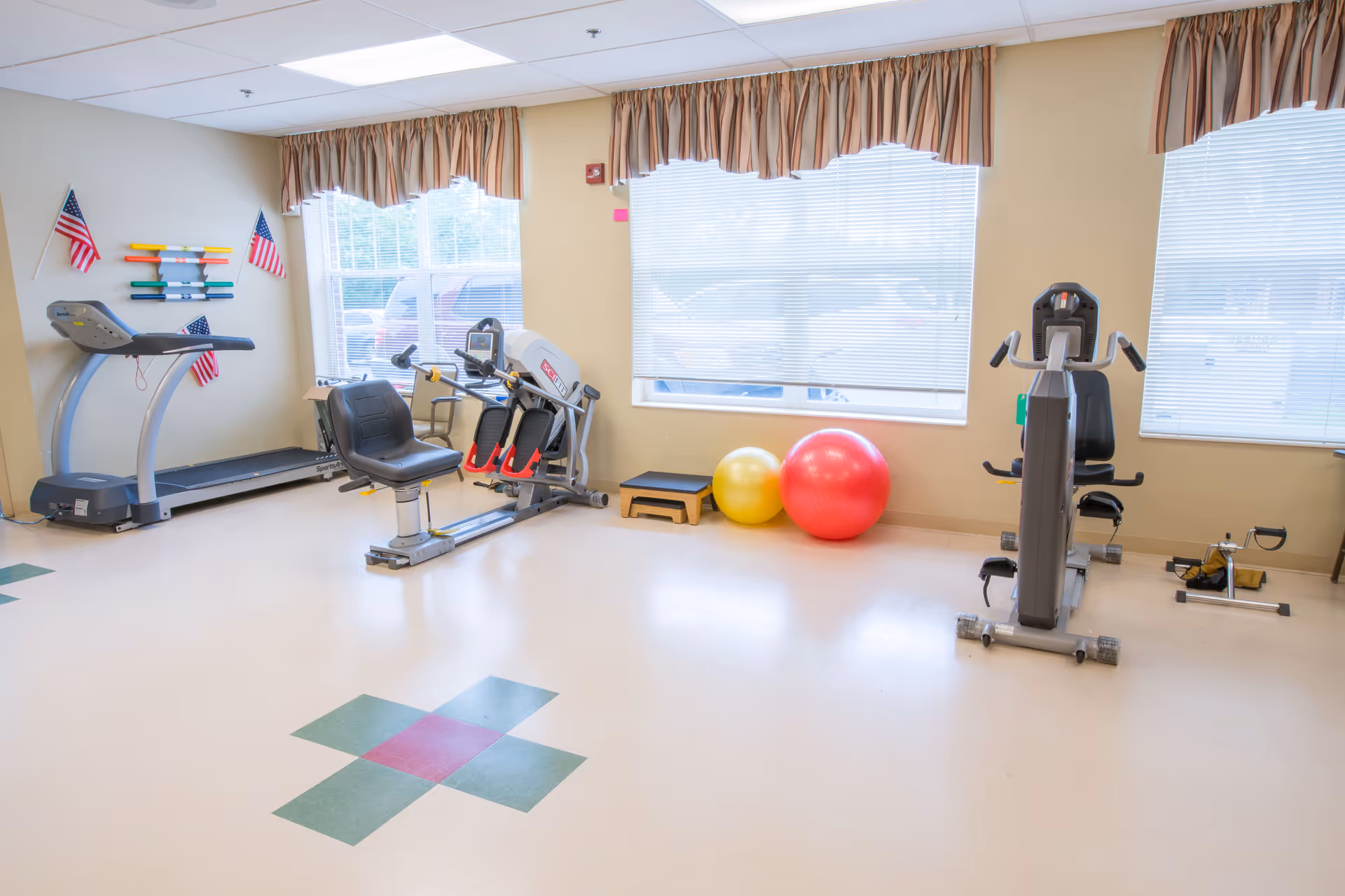 Bright exercise room with cardio machines, a treadmill, and two exercise balls by large windows.