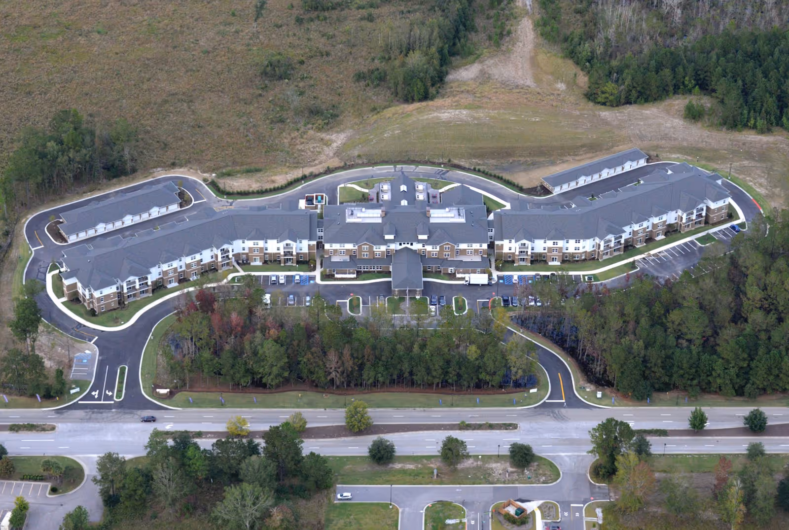 Aerial view of a large U-shaped retirement community building with surrounding parking lots, driveways, and wooded areas.
