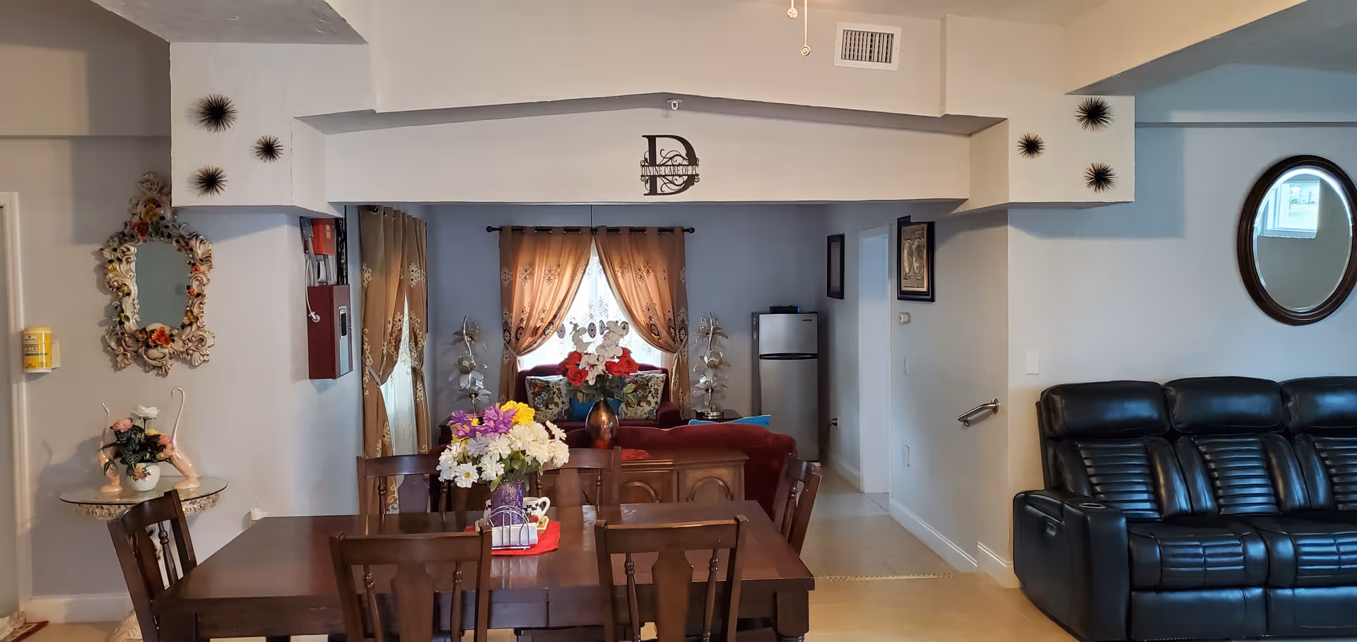Dining table with a floral centerpiece in an open-plan living area featuring sofas, curtains, and wall decor.