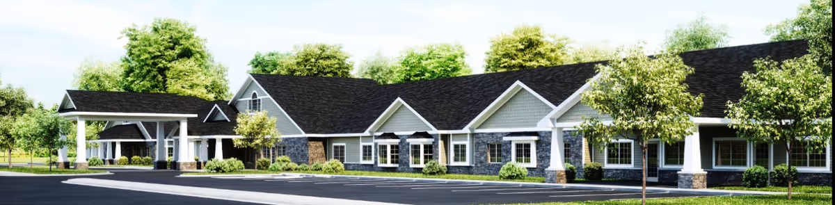 Exterior view of a single-story assisted living facility building with a covered entrance, multiple windows, and a landscaped area with trees and shrubs under a clear sky.