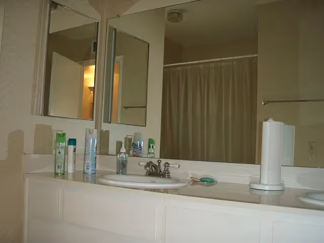 Bathroom vanity with double sinks, mirrors, toiletries, and a shower curtain in the background.