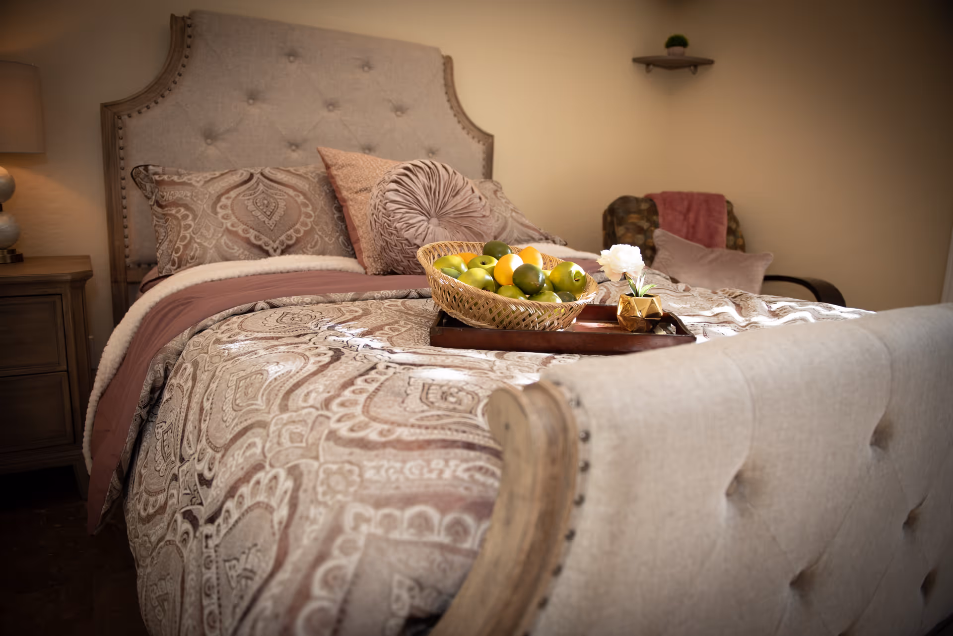Well-decorated bedroom with an upholstered bed, patterned bedding, decorative pillows, and a tray of fruit on the bed.