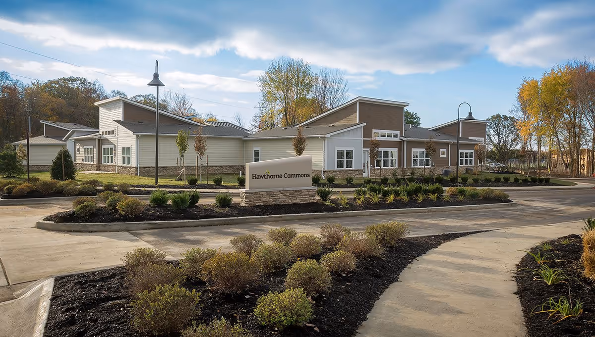 Exterior view of Hawthorne Commons facility with a modern single-story building surrounded by landscaped gardens and a curved driveway under a partly cloudy sky.