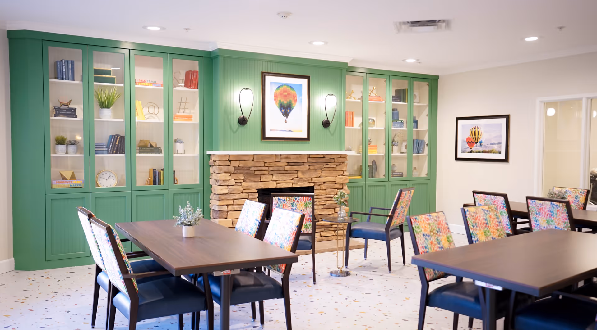 A colorful dining area with tables, chairs, a stone fireplace, and built-in shelves.
