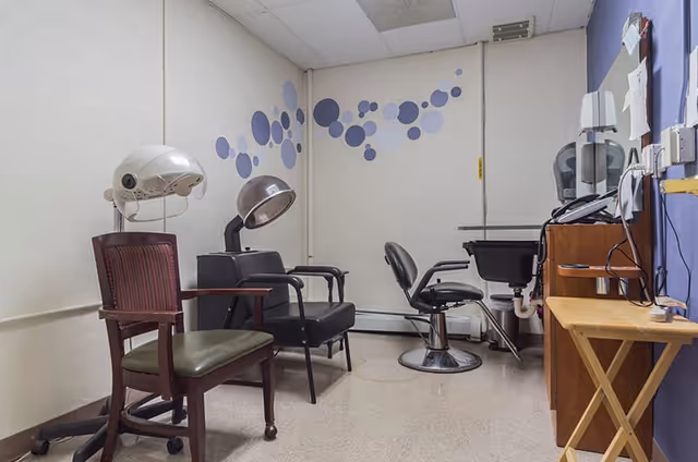 Small salon room with multiple styling chairs, hooded hair dryers, a wash basin and circular wall decals.