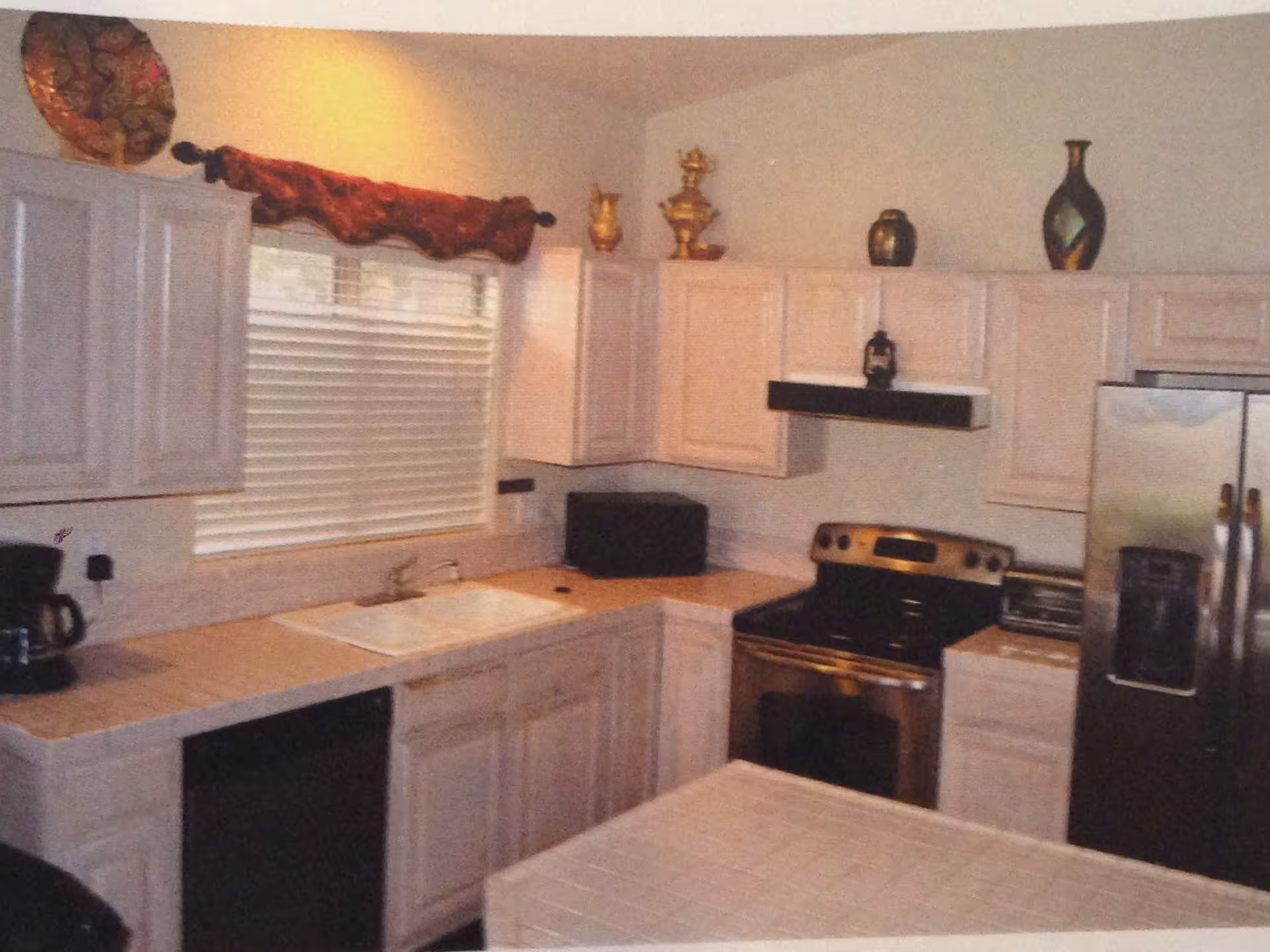 Kitchen interior with light wood cabinets, a sink under a window, stainless steel stove and refrigerator, and countertop appliances.