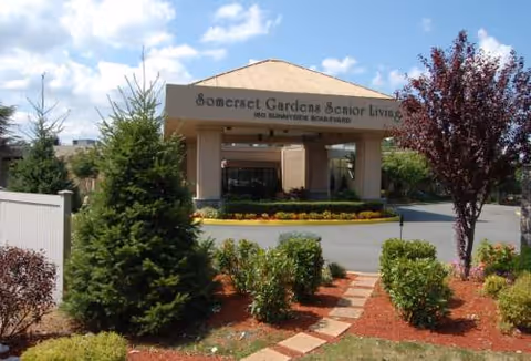 Exterior entrance of Somerset Gardens Senior Living with landscaped shrubs and a walkway.