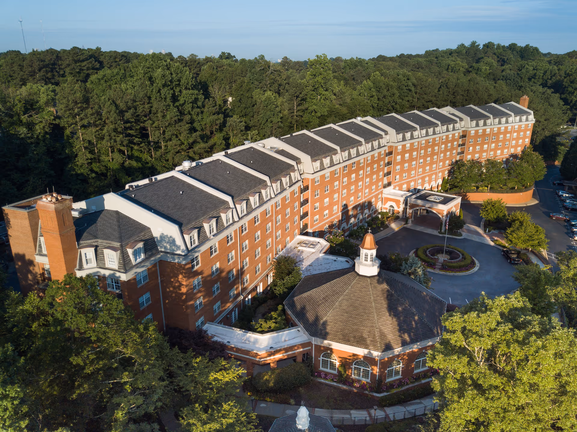 Aerial view of a long red-brick multi-story retirement building with a circular driveway and surrounding trees.