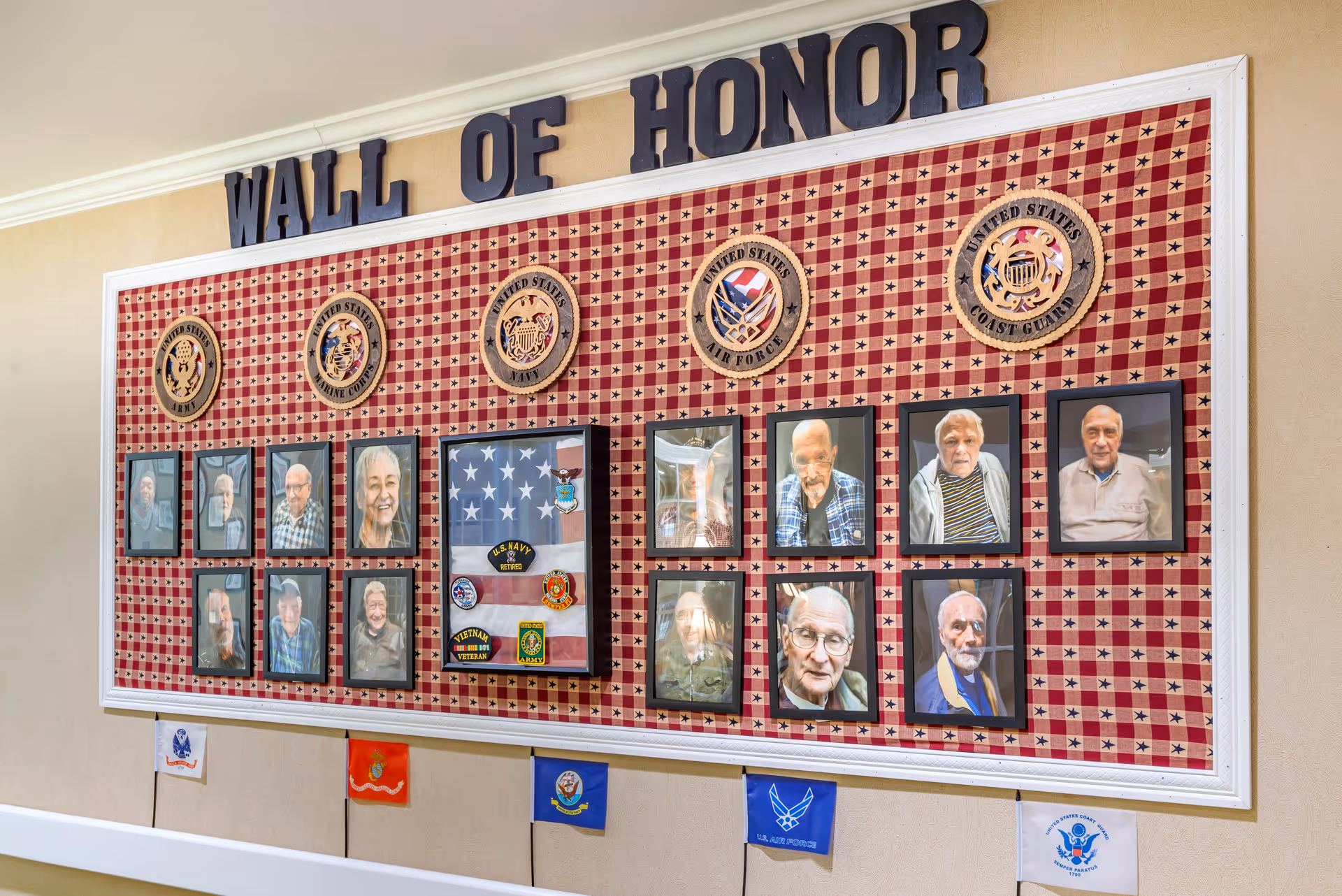 Indoor 'Wall of Honor' display board with framed photos of residents and military emblems and badges.