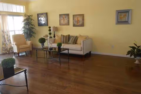 Bright living room with beige sofa, armchair, coffee table, plants, and wall art.
