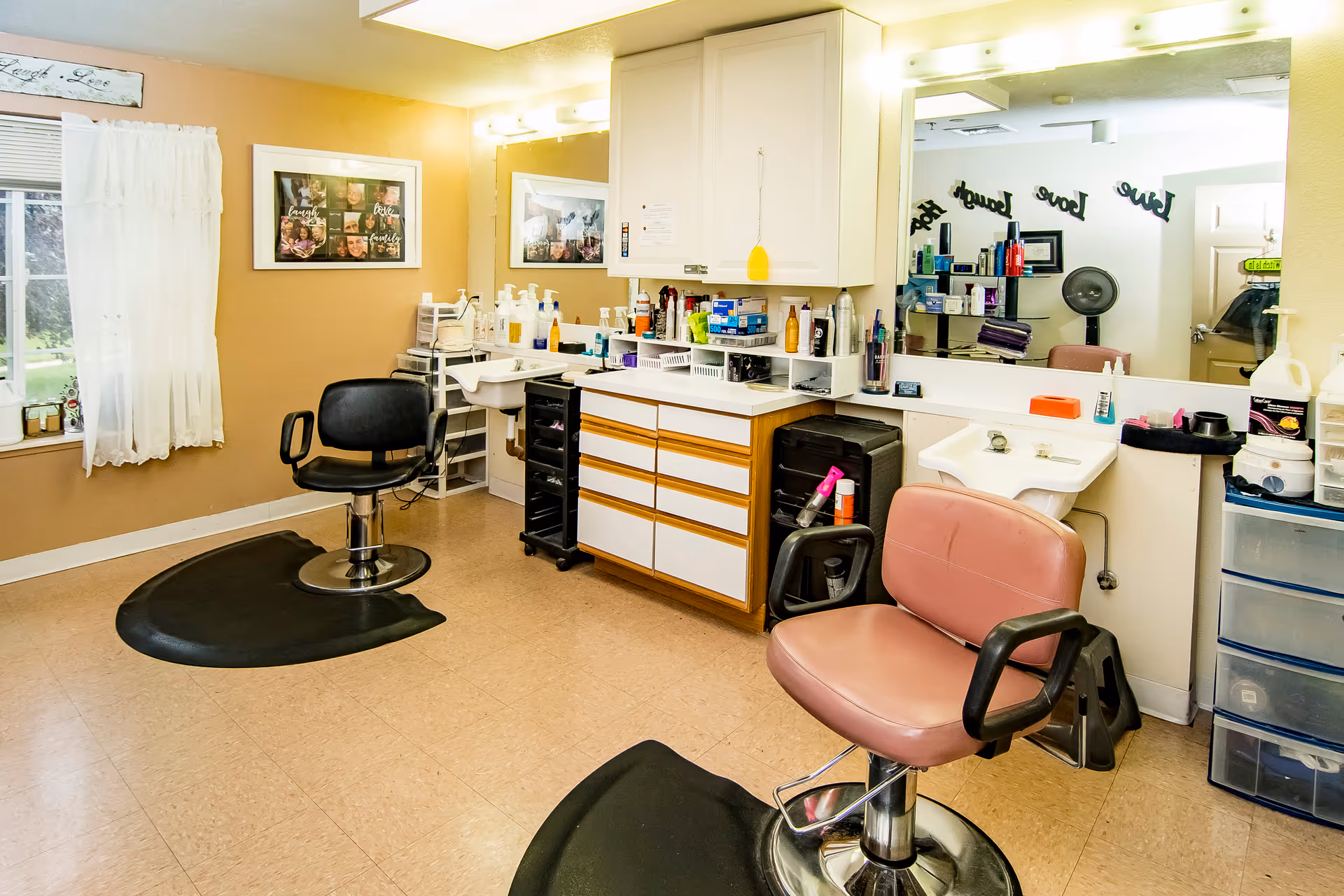 Small hair salon inside a senior living facility with two styling chairs, mirrors, sinks, and styling supplies.