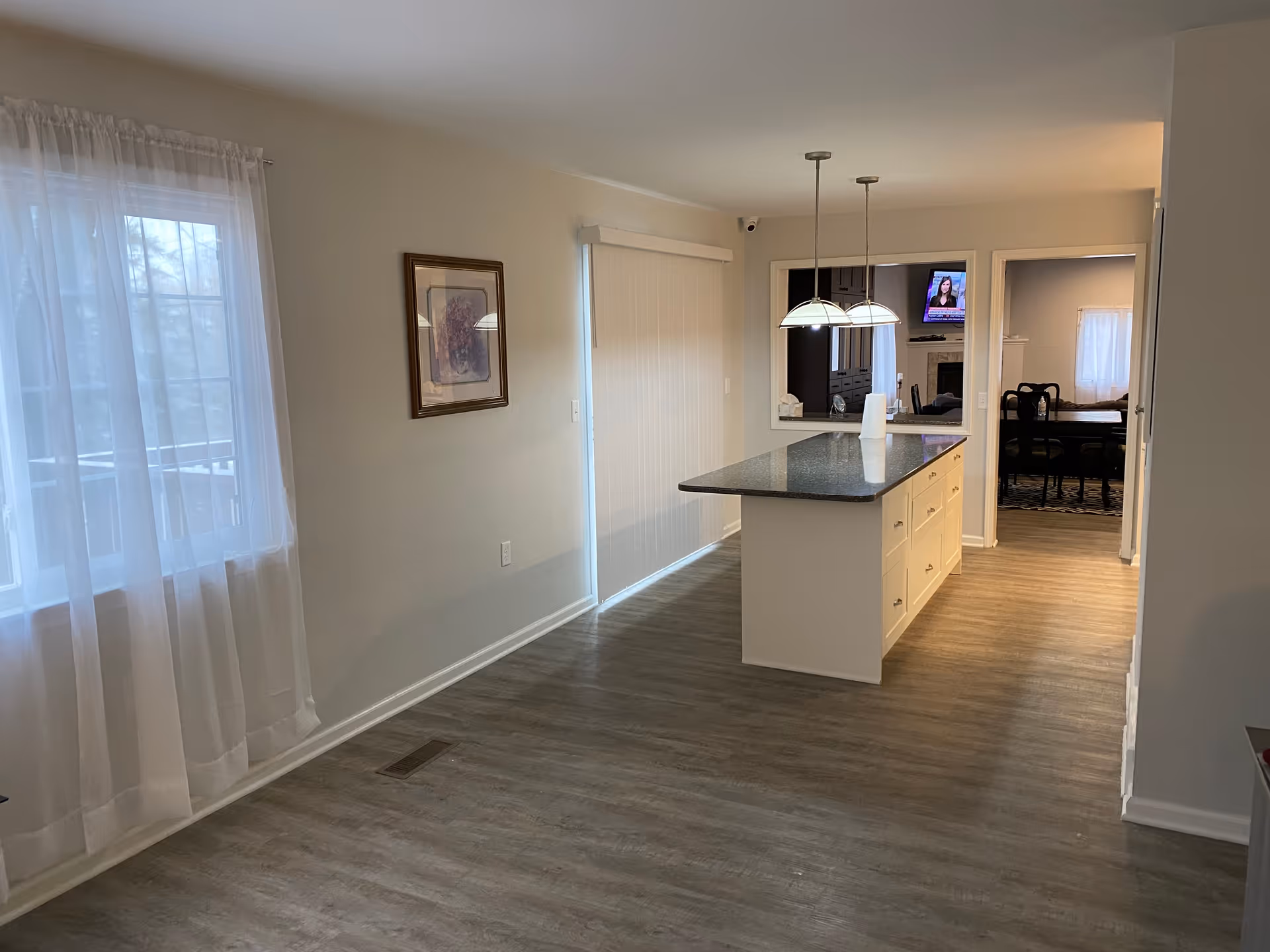 Bright open kitchen with a large island, pendant lights, and an adjacent dining area visible through a doorway.