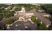 Aerial view of a senior living complex showing the main entrance, surrounding building wings, parking lot and trees.