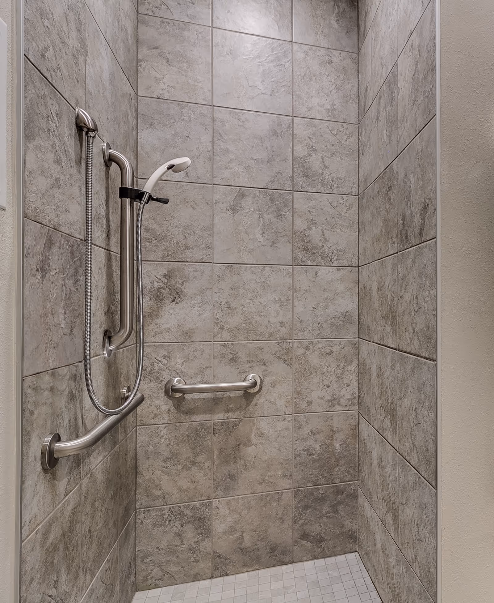 Tiled walk-in shower with a handheld showerhead and stainless steel grab bars.