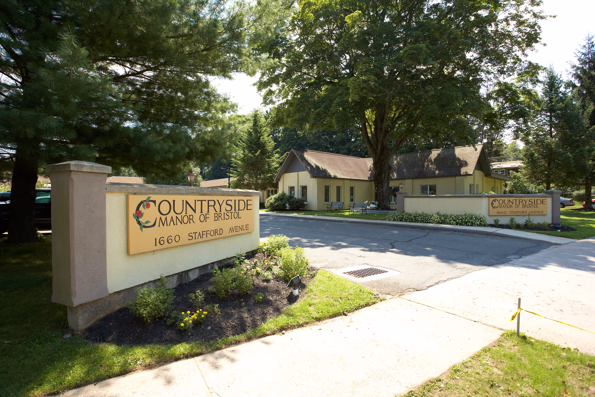 Entrance signs and front exterior of Countryside Manor of Bristol with driveway, landscaping, and trees.