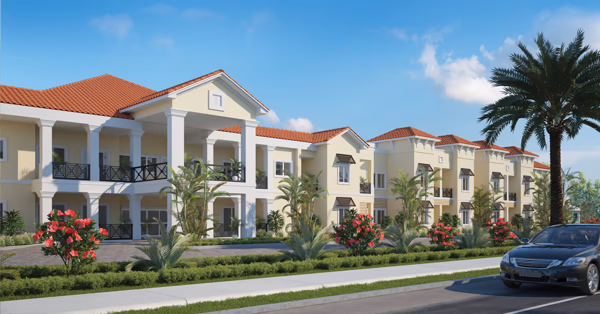 Two-story Mediterranean-style senior living building with balconies, palm trees, flowering shrubs, and a car parked on the street.