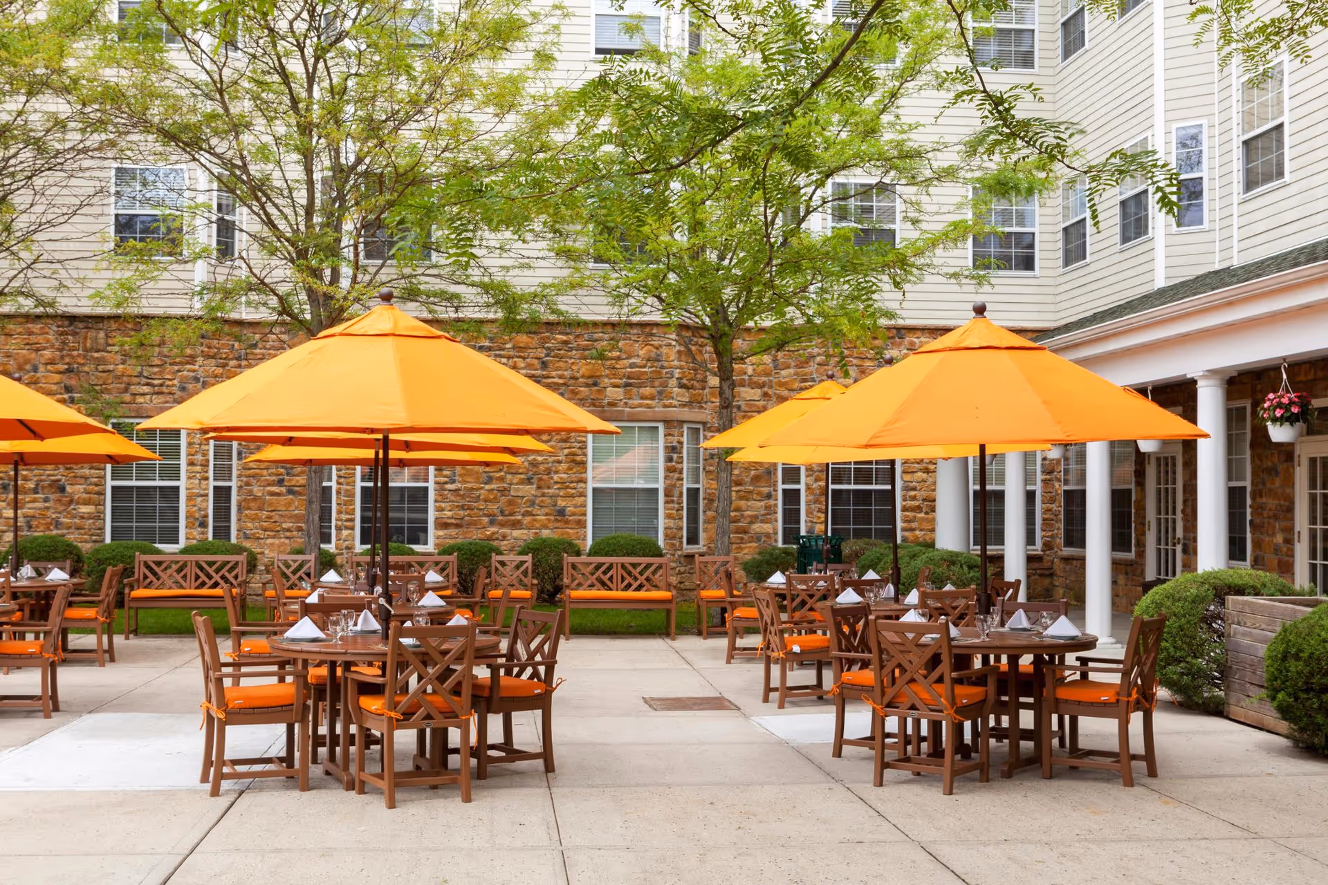Courtyard patio with orange umbrellas, wooden dining tables and chairs outside a senior living building.