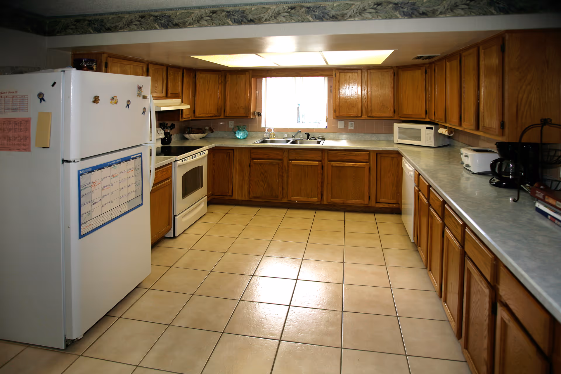 Spacious kitchen with tiled floor, oak cabinets, a white refrigerator and stove, and long countertops.