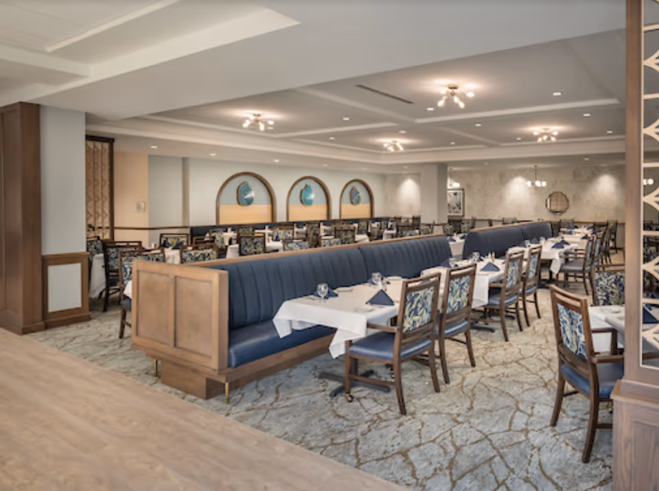 Spacious dining room with rows of tables, blue upholstered banquette seating, and wooden chairs set for service.