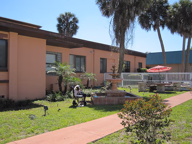 Sunlit courtyard of Savannah Court of Leesburg with fountain, palm trees, and patio seating