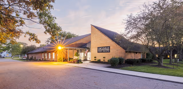 Front exterior of a brick, single-story senior care facility with a peaked roof and lit entrance sign reading 'Circleville Post Acute' at dusk.