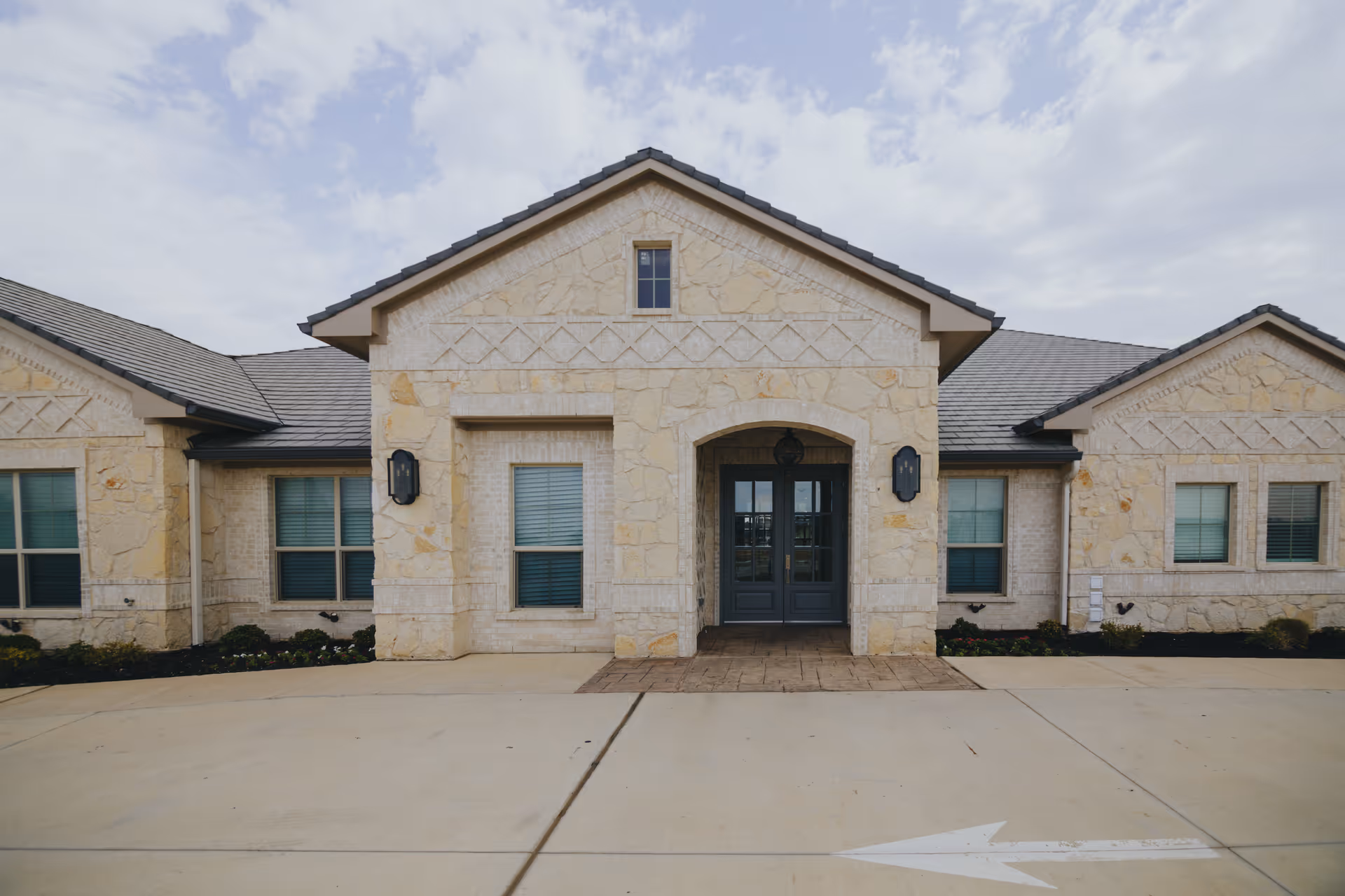 Stone-clad single-story building with a central arched entrance and double doors under a gabled roof.