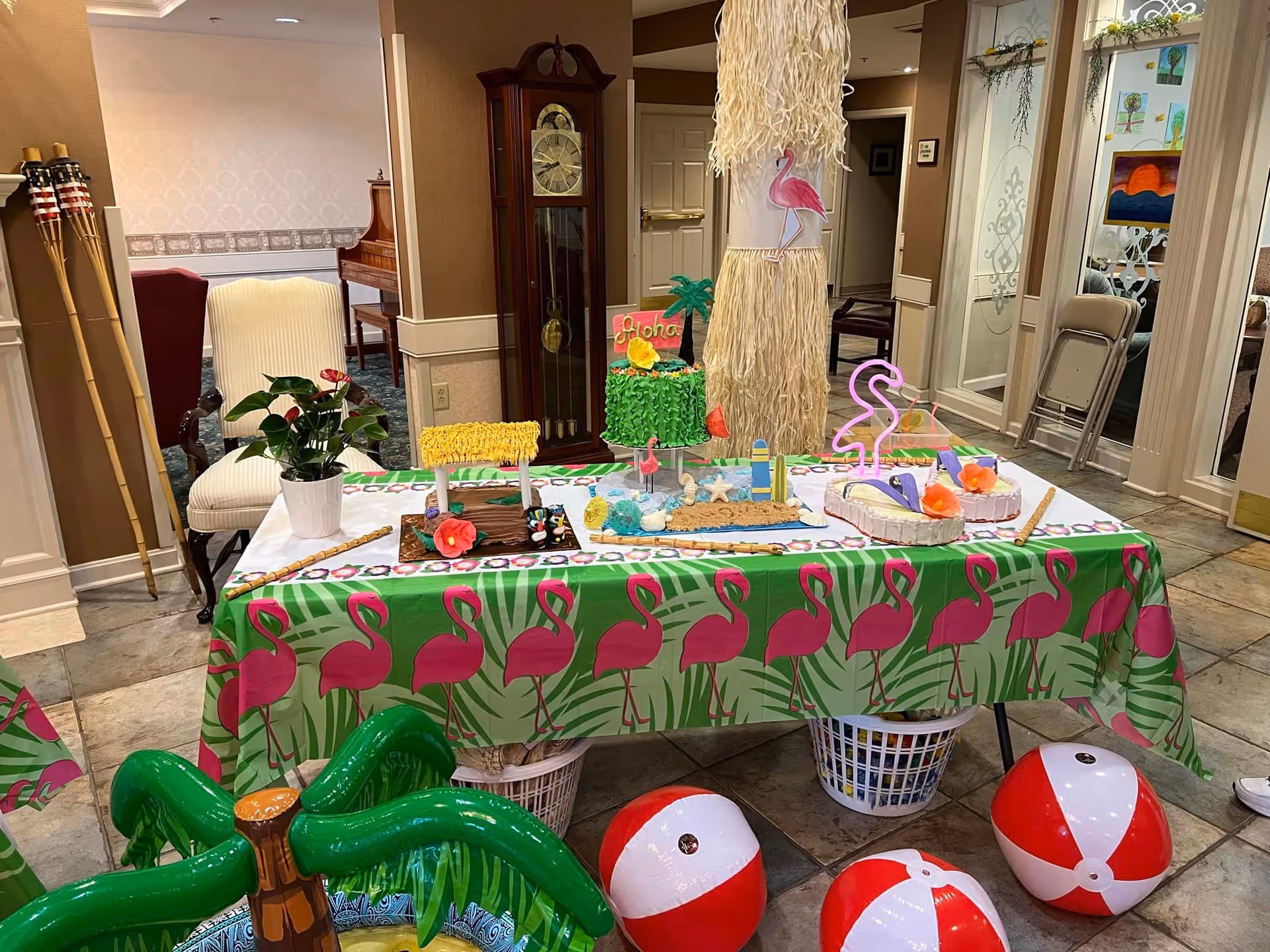 Indoor common room table decorated with flamingo-themed tablecloth, tropical party decorations and beach balls.
