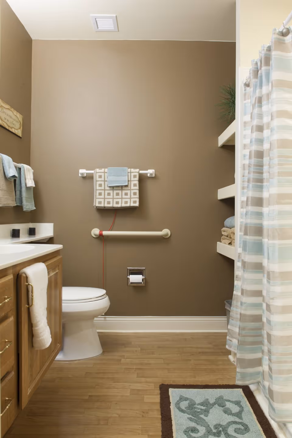 Small bathroom with a toilet, wooden vanity, towel racks, a grab bar, and a shower with a striped curtain.