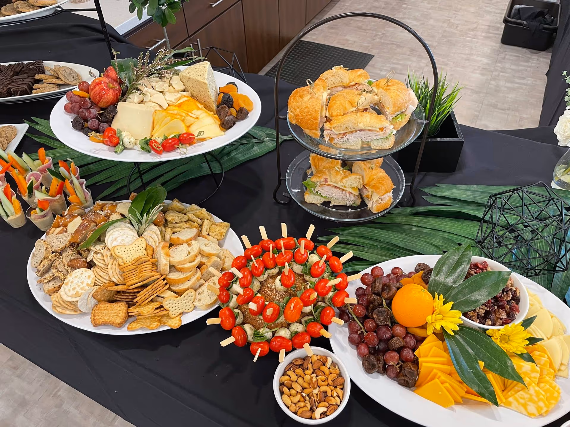 Buffet-style spread of cheeses, crackers, sandwiches, fruits, and nuts on a black table.