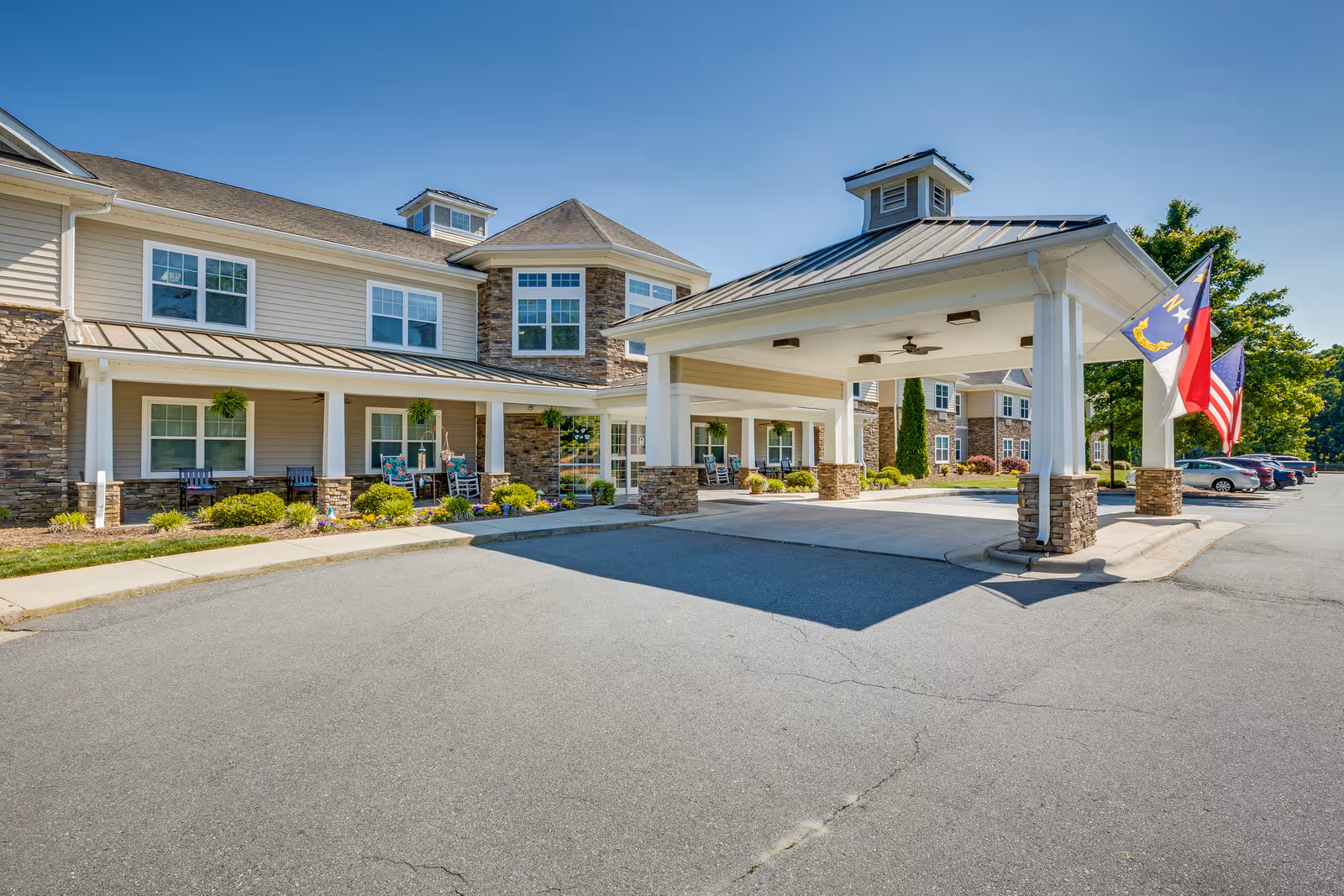 Senior living facility exterior with covered entrance, flags, and manicured landscaping.