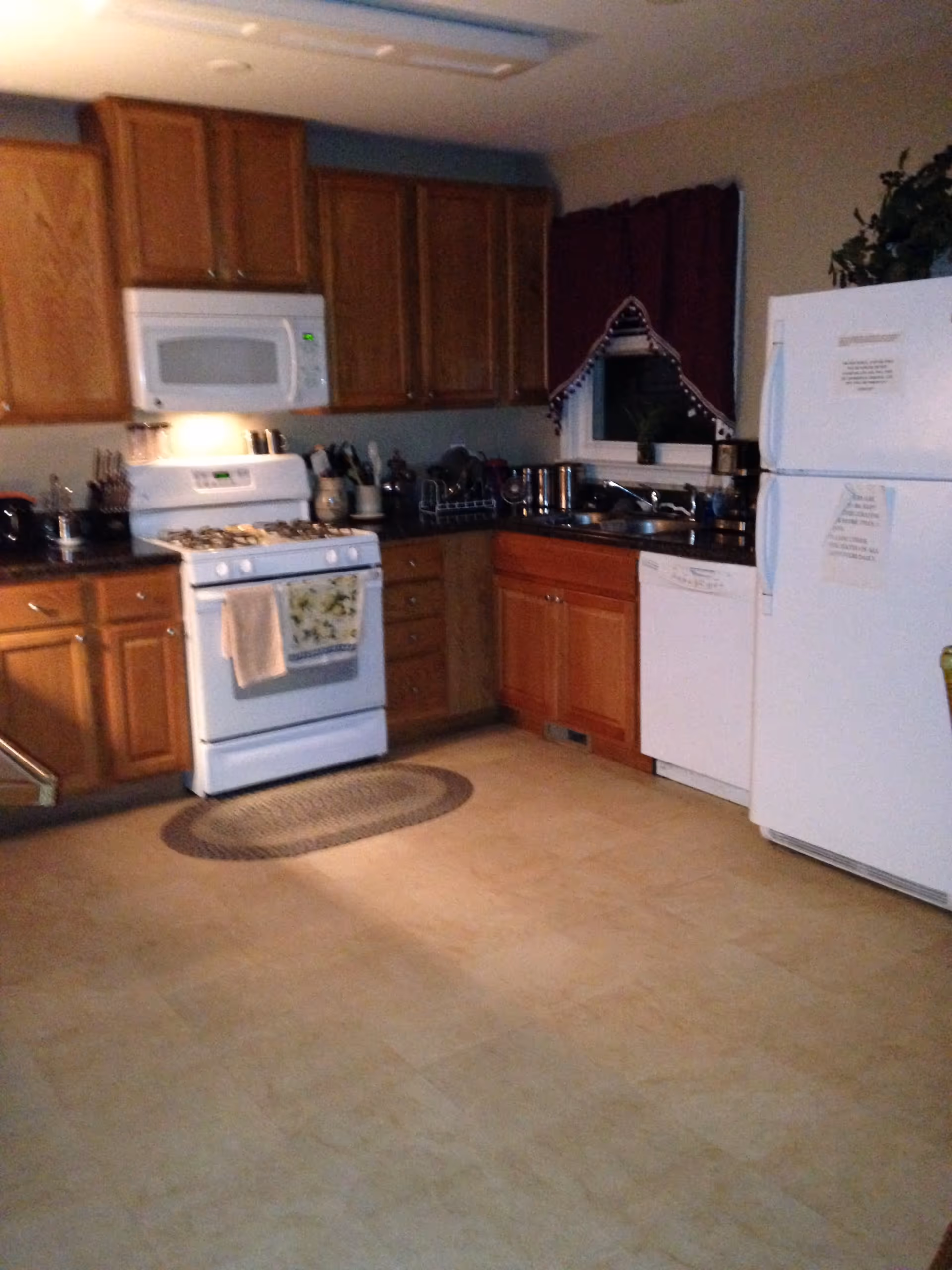A residential kitchen with oak cabinets, a white stove and microwave, a refrigerator, and a sink area.