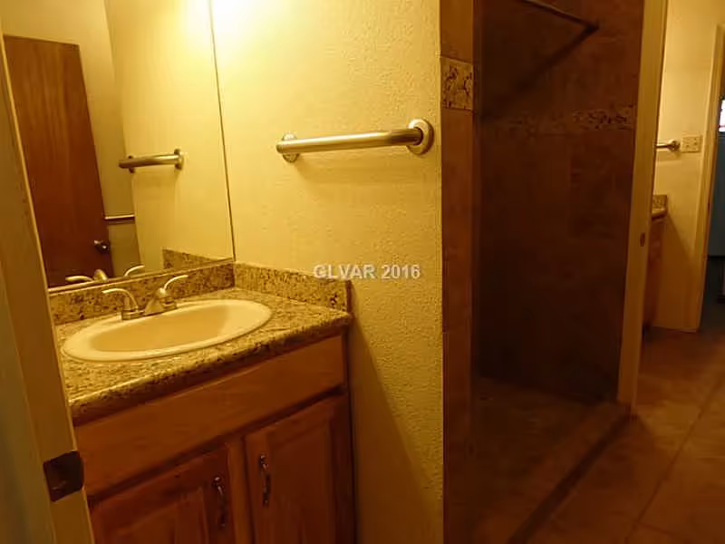 Small bathroom with a sink and granite countertop, mirror, towel bar, and a tiled walk-in shower.