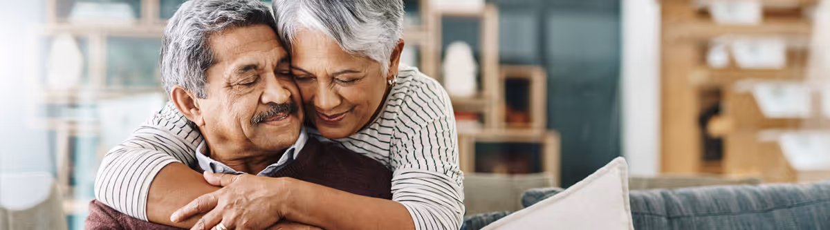A senior couple embraces on a couch in a cozy living room setting.