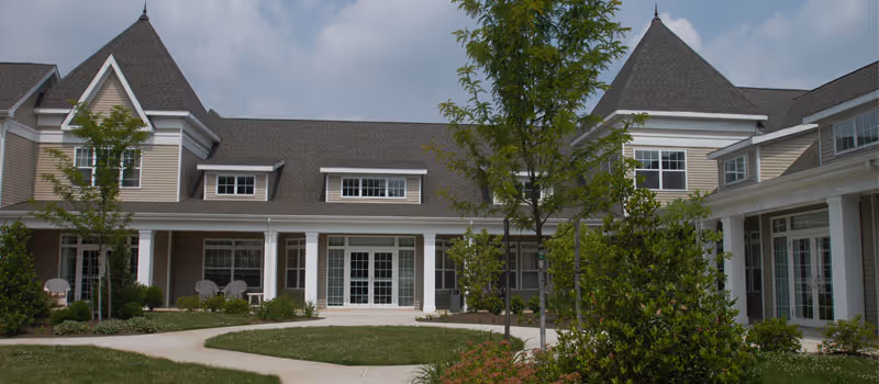 Front exterior of Stein Assisted Living building with a landscaped courtyard, walkways, and large windows.