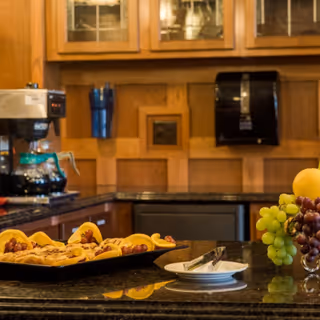 Granite countertop in a kitchen area with a tray of pastries, a bowl of grapes, a coffee maker, and wooden cabinets in the background.