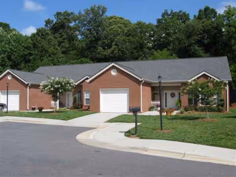 Brick senior living facility front exterior with garages and manicured lawn.
