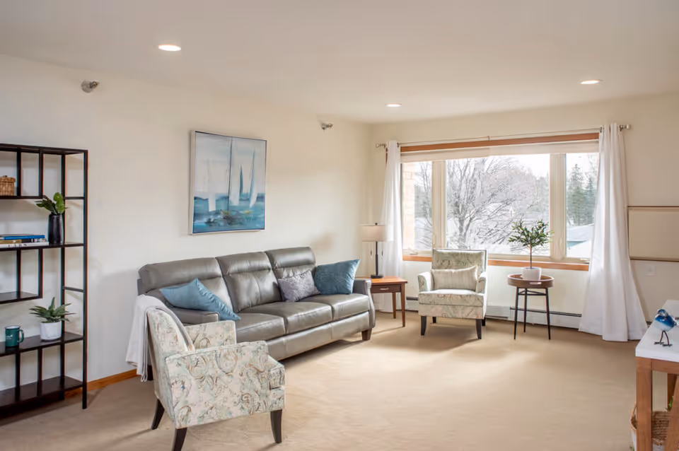 Bright living room with sofa, chairs, and large window overlooking winter trees.