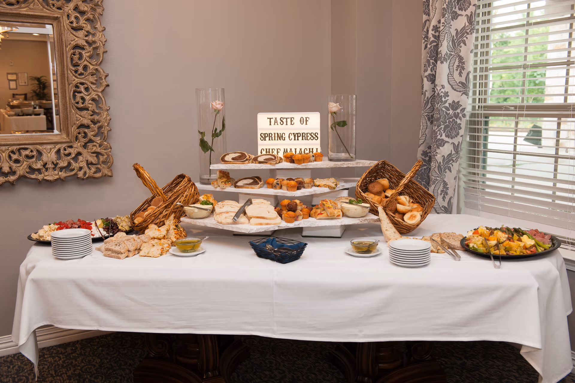 Buffet table with assorted breads, pastries, and fruit arranged on platters and tiered stands in a dining room.
